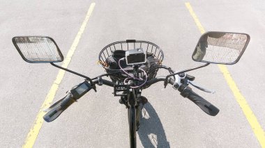 Güneşli yaz gününde parkta elektrikli bisiklet dümeni ya da dümen. Yukarıdan vurulmuş. Çan, fren, sürat anahtarı ve güç kontrol cihazı ve aynalı e-bisiklet direksiyonu manzarası.