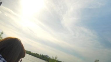 Bir kadın kum üzerinde günbatımında nehir kenarında oturur ve cep telefonu görünüyor