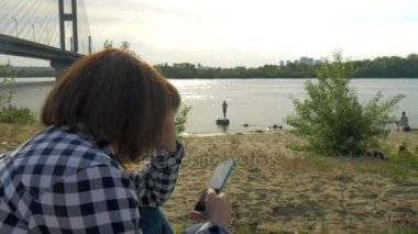 Bir kız açık havada yere oturur ve sosyal ağların telefondaki iletileri okur