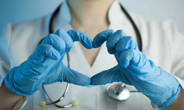 Doktor kadın Beyaz önlük ile kalp parmaklarının arasından gösterir