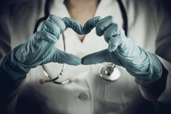 Doctor woman with a white lab coat shows heart from the fingers