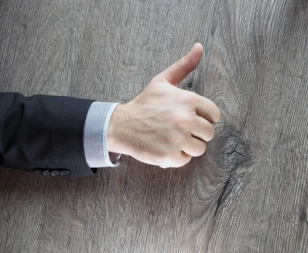 Businessman showing OK sign with his thumb up isolated with dark wooden background. Success business deal. Businessman in a suit shows a sign ok fingers of two hands
