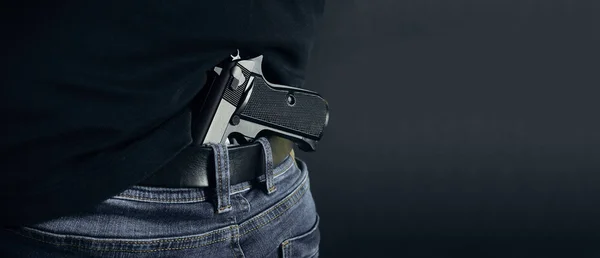 Terrorist thief man holding gun in his hand. Hidden gun. Isolated on dark background. copy space