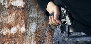 Elinde bir silah siyah kazak ve mavi jeans ile kopya alanı ile adam katil. Onun tutan adam onun arka siyah bir tabanca ver. Paslı metal arka plan kopya alanı ile izole.
