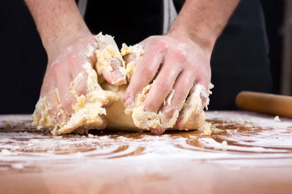 Чоловічий пекар замішує тісто на борошняному критому столі — стокове фото