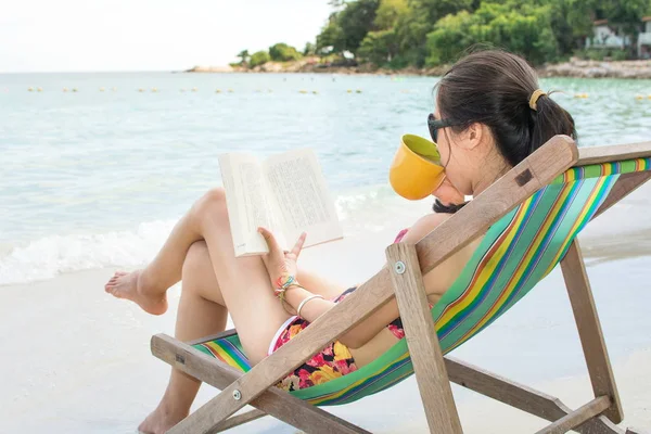 Girl reading a book in sunbed by the sea — Stock Photo, Image