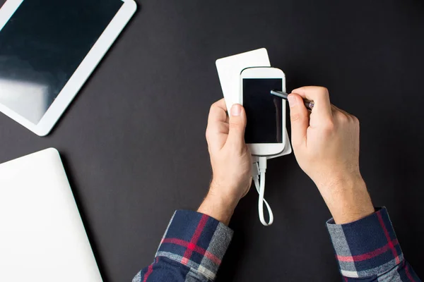 Manliga händer som håller en vit mobiltelefon ansluten till en Powerbank — Stockfoto