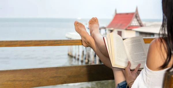 Girl reading book on the balcony with seaside view — Stock Photo, Image