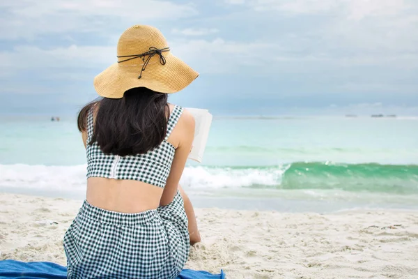 Flicka som läser en bok på en sandstrand — Stockfoto