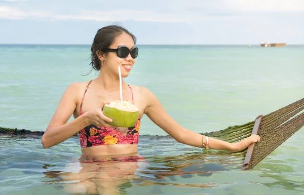 Девушка с кокосом на тропическом качелях на пляже — стоковое фото
