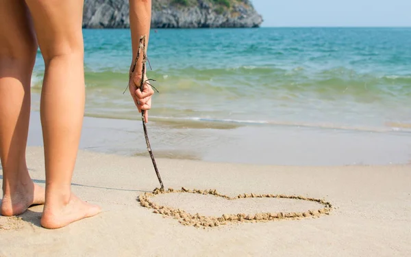 Girl drawing a hearth shape on the beach — Stock Photo, Image