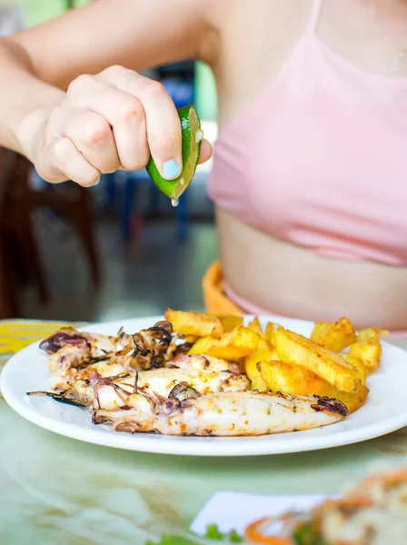 Weibliche Hand drückt Limette auf gegrillten Tintenfisch mit Pommes — Stockfoto