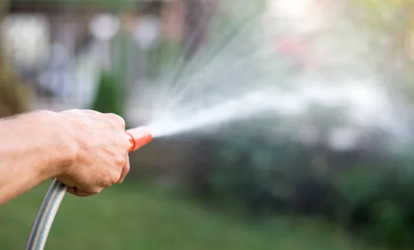 Man watering flowers with a hose — Stock Photo, Image