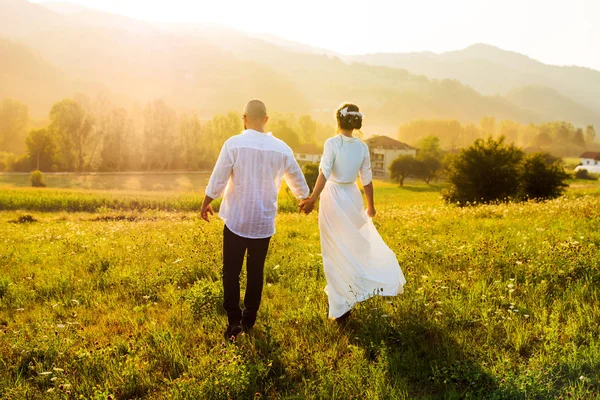 Casal caminhando no campo com vista para o pôr do sol — Fotografia de Stock