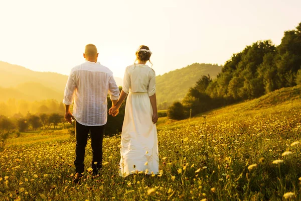 Casal caminhando no campo com vista para o pôr do sol — Fotografia de Stock