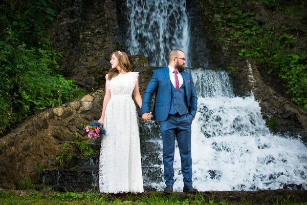 Couple de mariage debout devant une cascade — Photo