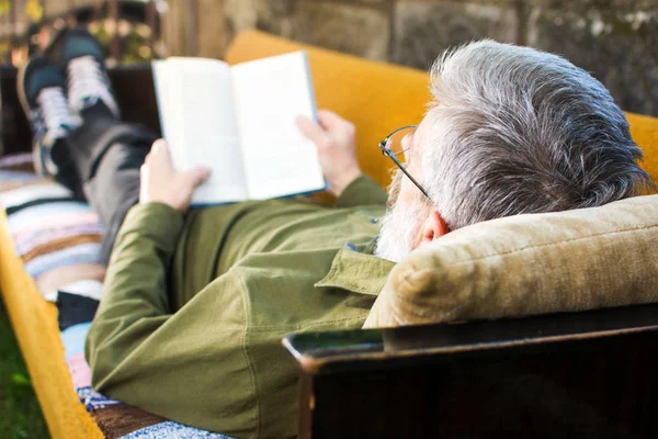 Homem sénior lendo um livro no quintal — Fotografia de Stock