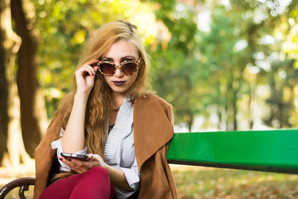 Menina na moda sentada em um banco de parque — Fotografia de Stock