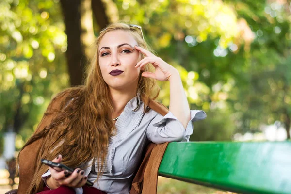 Модная девушка сидит на скамейке в парке — стоковое фото