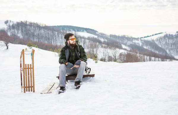 Człowiek siedzi na szczycie góry z drewniane sanki — Zdjęcie stockowe