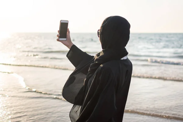 Женщина в хиджабе фотографирует на пляже — стоковое фото