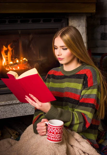 Girl reading by the fireplace sitting on the floor — Stock Photo, Image