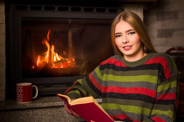 坐在地板上的壁炉边看书的女孩 — 图库照片