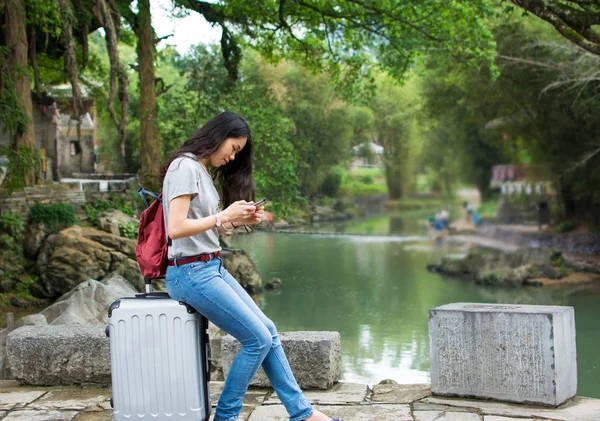 Dívka sedící na kufr a hraje ji telefon v stunnin — Stock fotografie