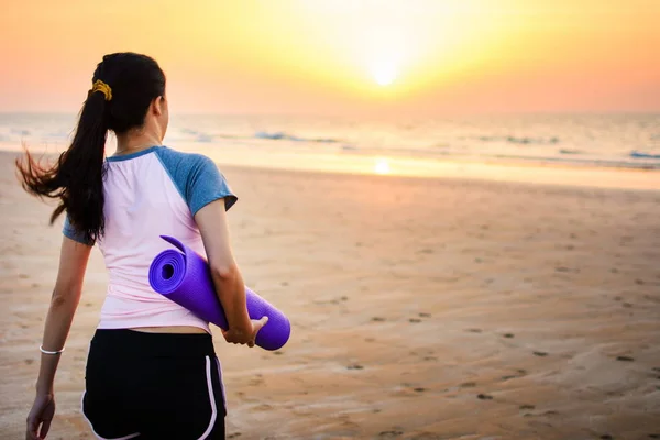 Flicka med yogamatta på stranden — Stockfoto