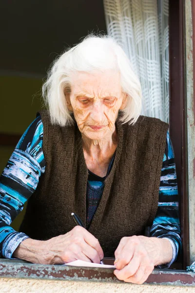 Mulher sênior assinando cheque de aposentadoria em casa — Fotografia de Stock