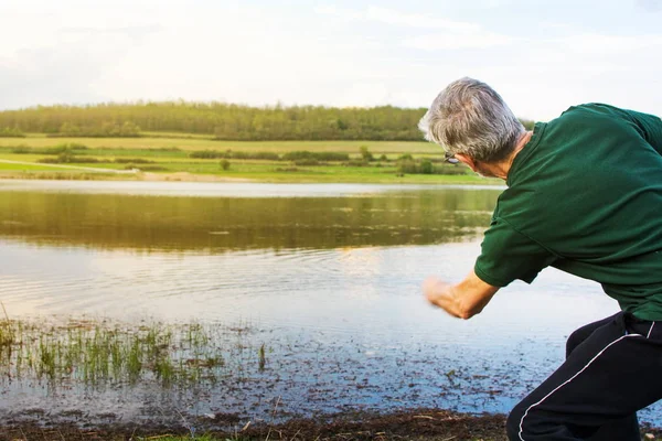 Hombre mayor jugando a la piedra saltando en un lago — Foto de Stock