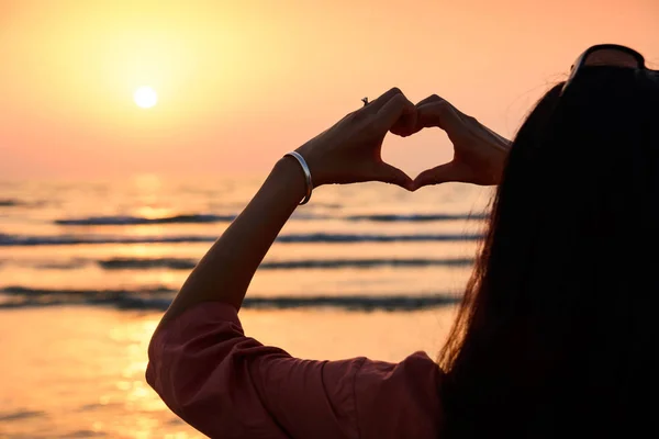 Menina fazendo forma de coração com as mãos no pôr do sol — Fotografia de Stock