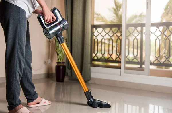 Woman vacuuming the living room floor with cordless vacuum cleaner