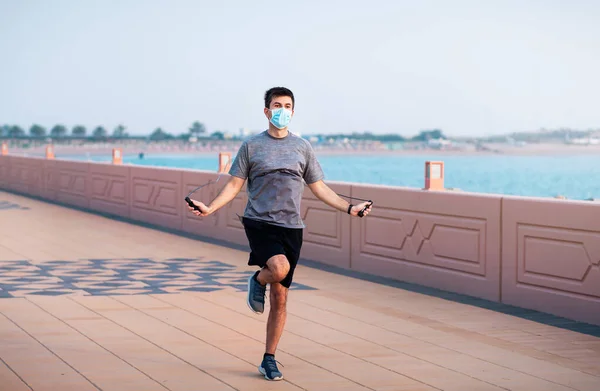 Man exercising with a jumping rope and wearing protective surgical mask outdoors