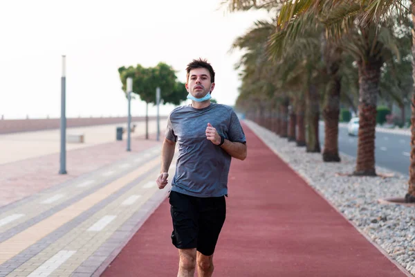 Man jogging on the running track wearing protective surgical mask