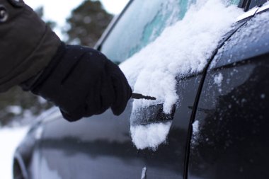 bir adam bir arabanın kapısını kışın bir anahtarla açarak.