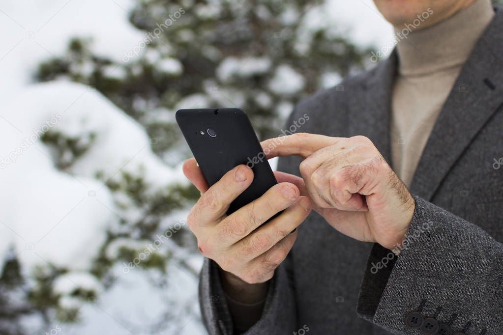 close-up of a businessman in winter in the forest with a phone in a gnome cap