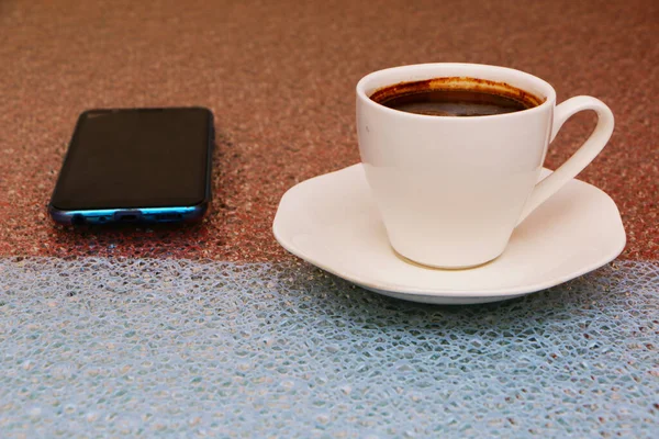 Smartphone a šálek kávy na mokrém červenomodrém stole. — Stock fotografie
