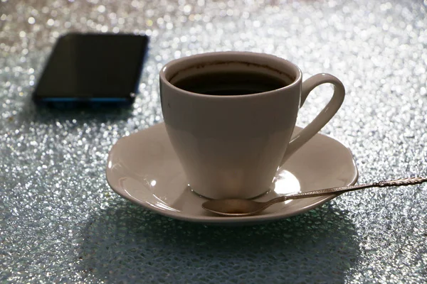 Copo com café e um smartphone à noite na mesa . — Fotografia de Stock