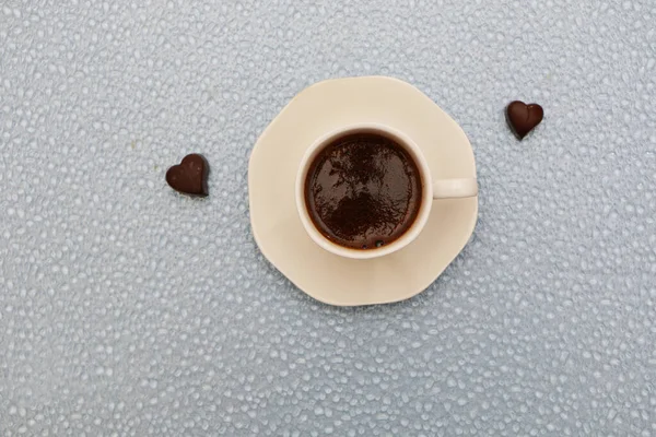 Close-up - a cup of coffee, next to two heart-shaped chocolates. — Stock Photo, Image
