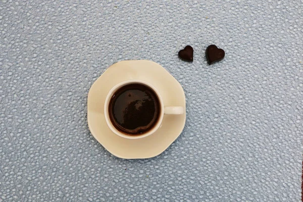 Close-up - a cup of coffee, next to two heart-shaped chocolates. — Stock Photo, Image