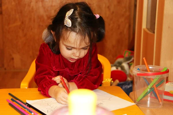 Маленькая девочка в красной платине рисует цветными карандашами — стоковое фото
