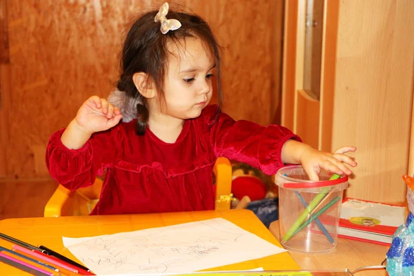 Een klein meisje gekleed in rood platina tekent met gekleurde potloden — Stockfoto