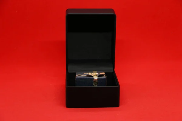 Black gift box for jewelry on a display case. Bright red background