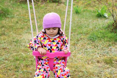 Kendini izole etme salgını sırasında açık bir alanda oynayan bir çocuk. Çocuklar okulda ya da anaokulunda oynarlar. Renkli salıncakta hareketli bir çocuk. Küçük kız sallanıyor
