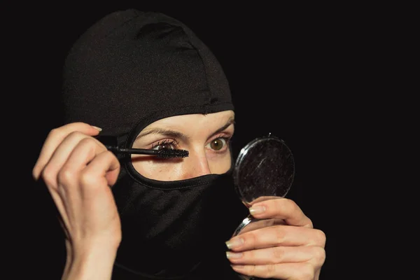 Rapariga criminosa. A menina em uma máscara preta pinta pestanas . — Fotografia de Stock