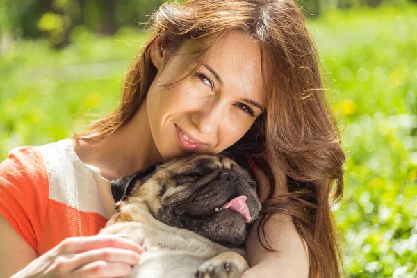 Perro de la raza Pug. Una chica está paseando a un perro en un césped verde . — Foto de Stock