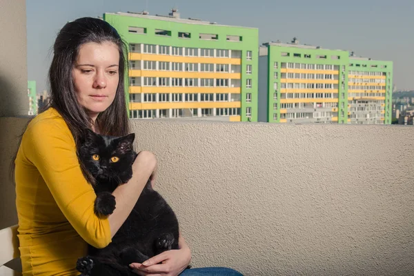 Ein Mädchen mit schwarzer Katze blickt vom Balkon auf ein neues Gebäude — Stockfoto