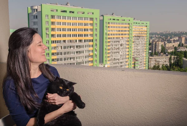 Ein Mädchen mit schwarzer Katze blickt vom Balkon auf ein neues Gebäude — Stockfoto