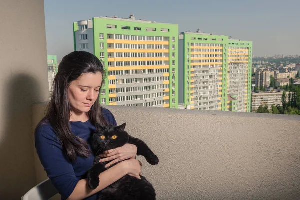 Ein Mädchen mit schwarzer Katze blickt vom Balkon auf ein neues Gebäude — Stockfoto